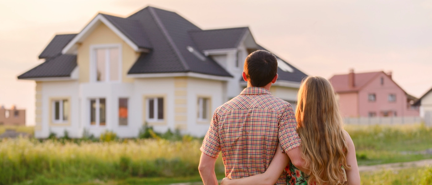 A couple holding each other and looking at a house in the near distance
