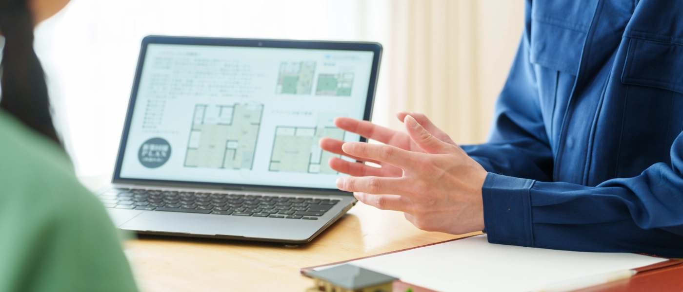 Two people discussing next to a computer with blueprints displayed on it.