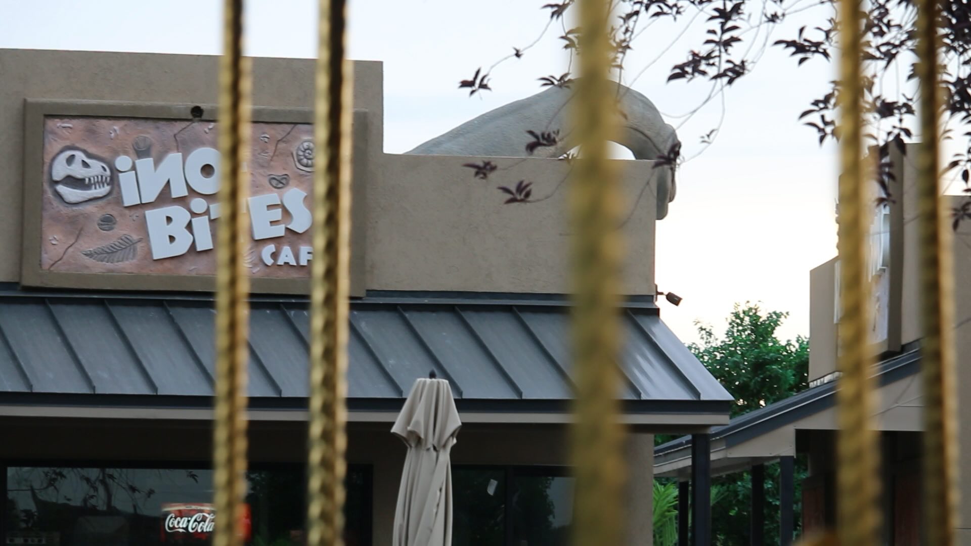 A building with a sign that says 'Dino Bites'. In the background is a large fake dinosaur.